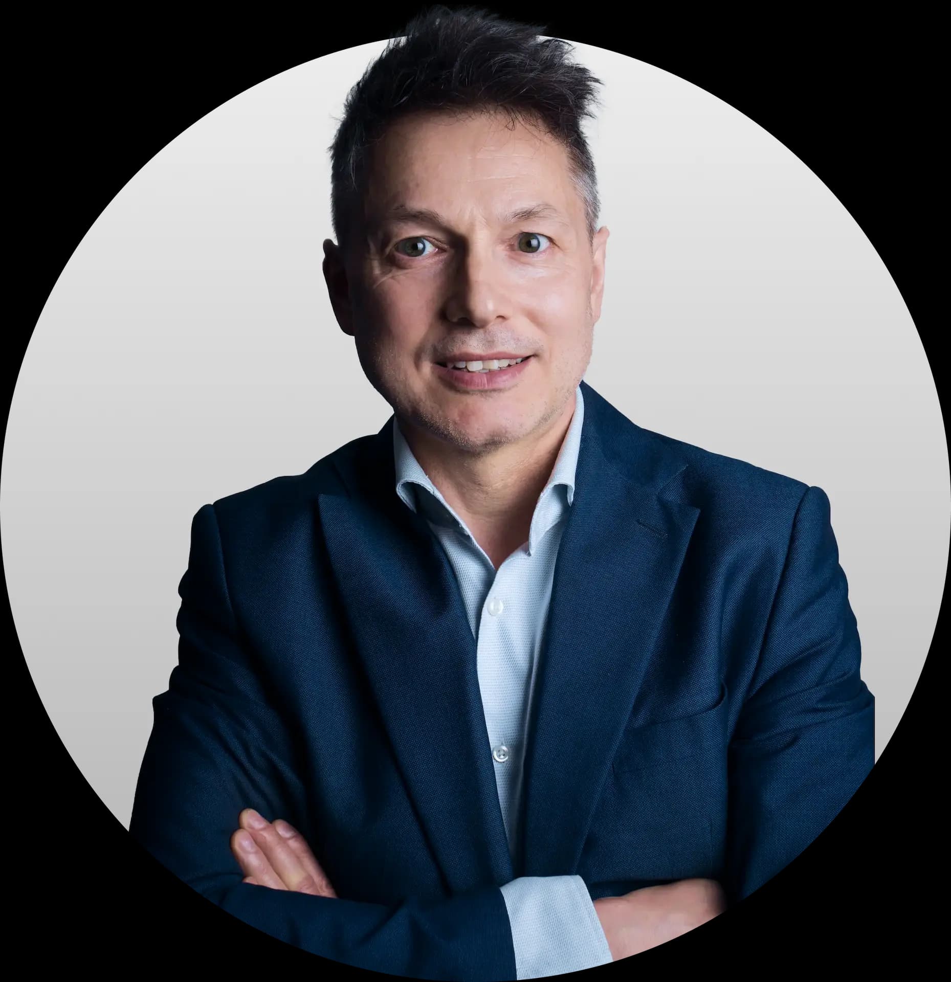 Zdjęcie uśmiechniętego Janusza Lisa - mężczyzny o krótkich, ciemnych włosach, ubranego w granatową marynarkę i błękitną koszulę, z założonymi rękoma.